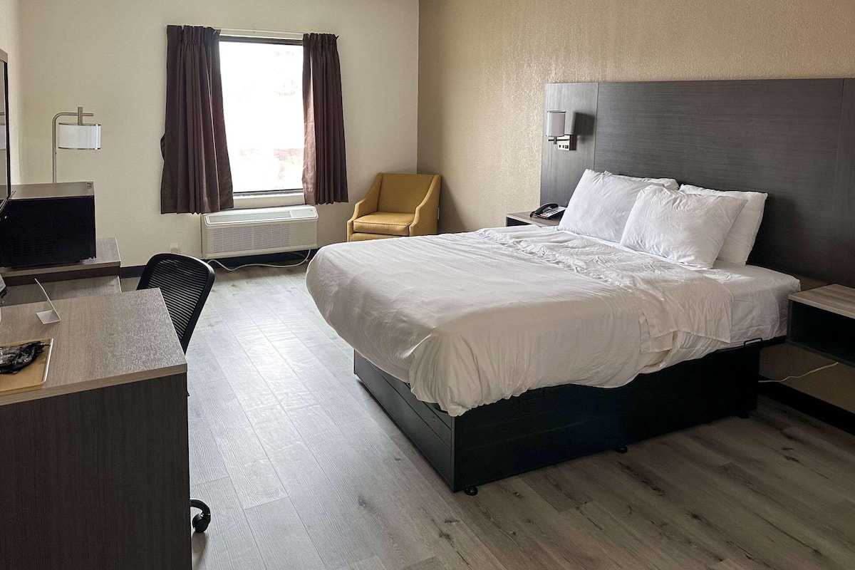 Une chambre d’hôtel avec un lit, un bureau, une chaise et une fenêtre avec des rideaux.