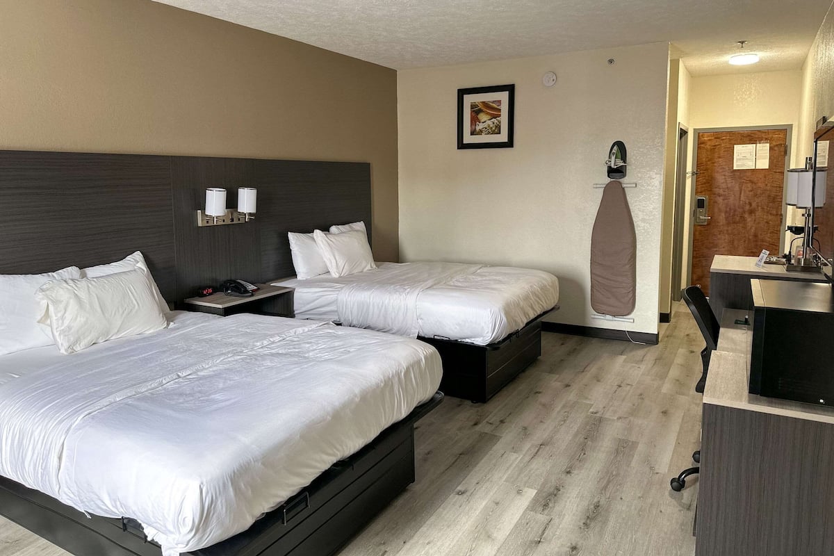 Une chambre d’hôtel avec deux lits, un bureau, une chaise, une armoire et un miroir.