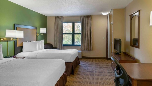 A hotel room with two beds, a desk with a television, a mirror, and a window with curtains. - Extended Stay America Suites Detroit Canton (Canton)