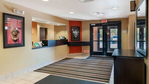 A hotel reception area with a reception desk, a framed artwork, an exit sign, and a striped carpet. - Extended Stay America Suites Detroit Canton (Canton)