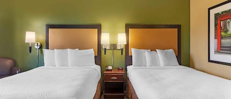 A hotel room with two beds, each with a headboard, bedside lamps, and a nightstand with a clock.