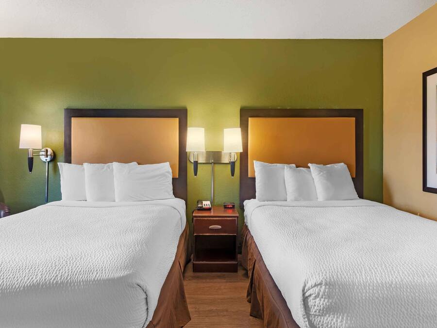 Quarto de hotel com duas camas, cada uma com cabeceira, abajures e mesa de cabeceira com relógio.