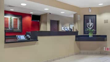 A hotel reception area with a red wall, a reception desk, a mounted TV, and an exit sign.