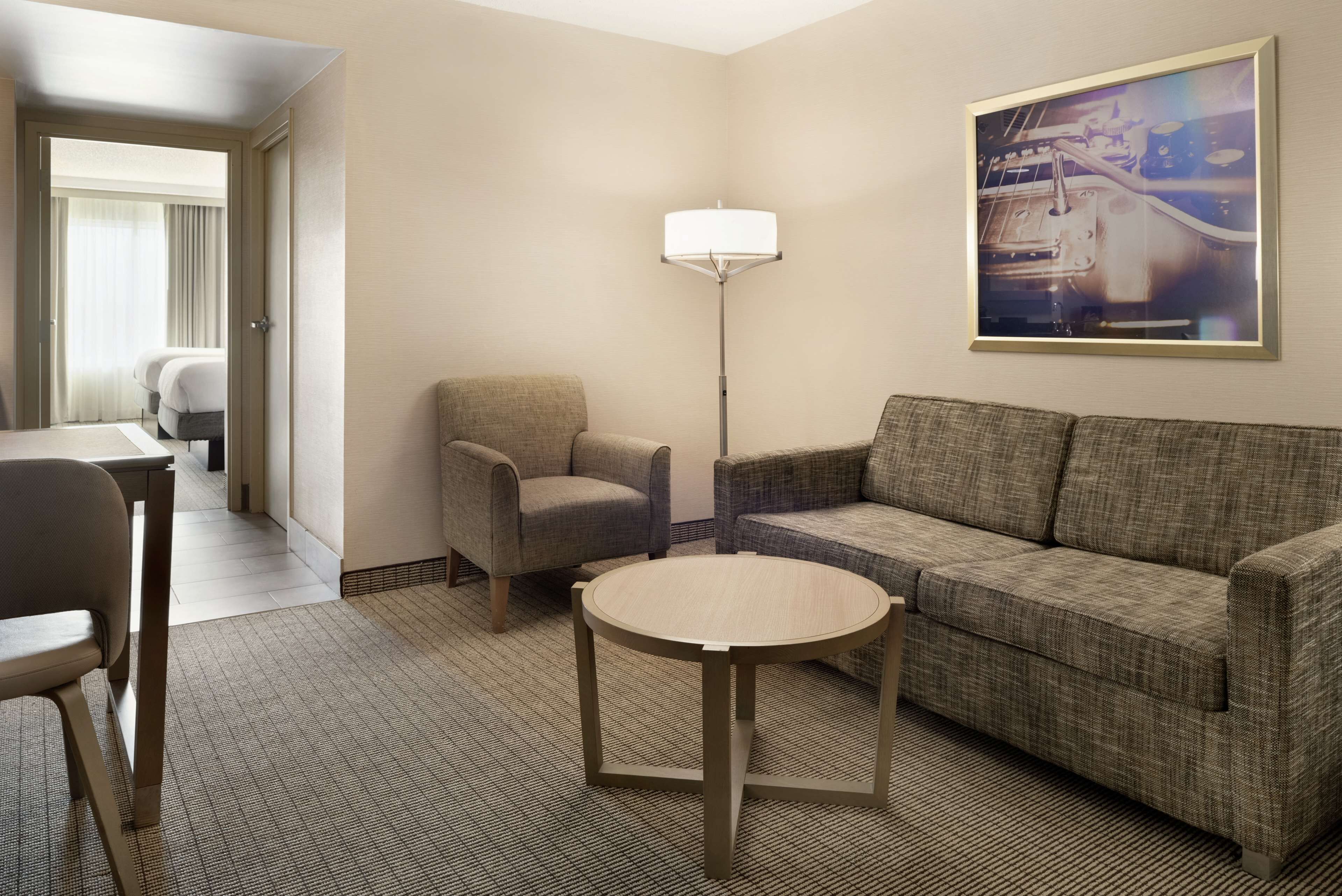 Habitación de hotel con sofá, sillón, mesa redonda y lámpara de pie.