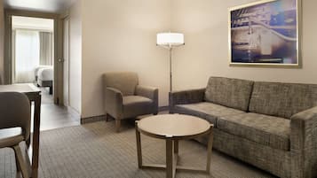 Habitación de hotel con sofá, sillón, mesa redonda y lámpara de pie.