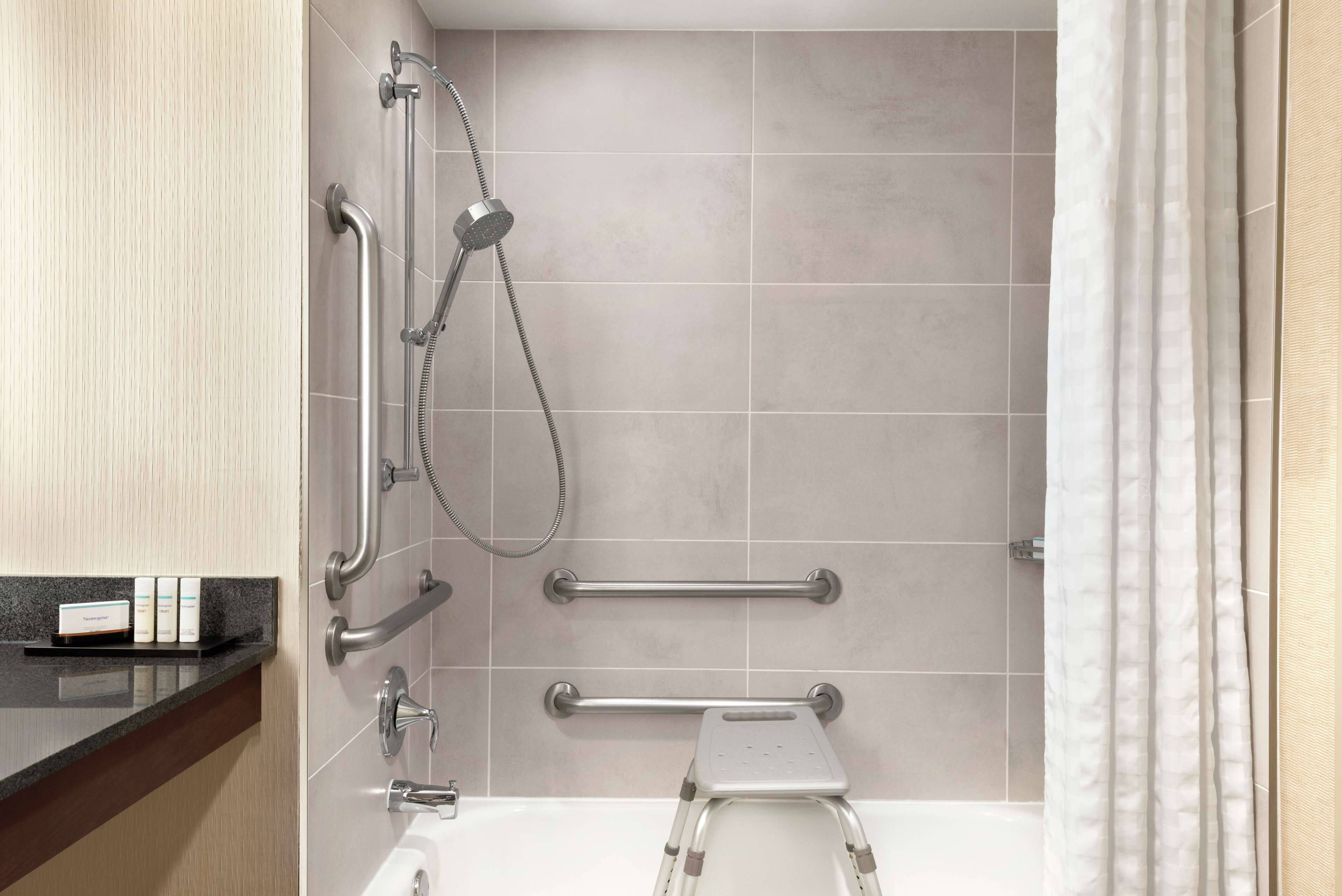 A modern bathroom with a shower, grab bars, a step stool, and a towel rack.