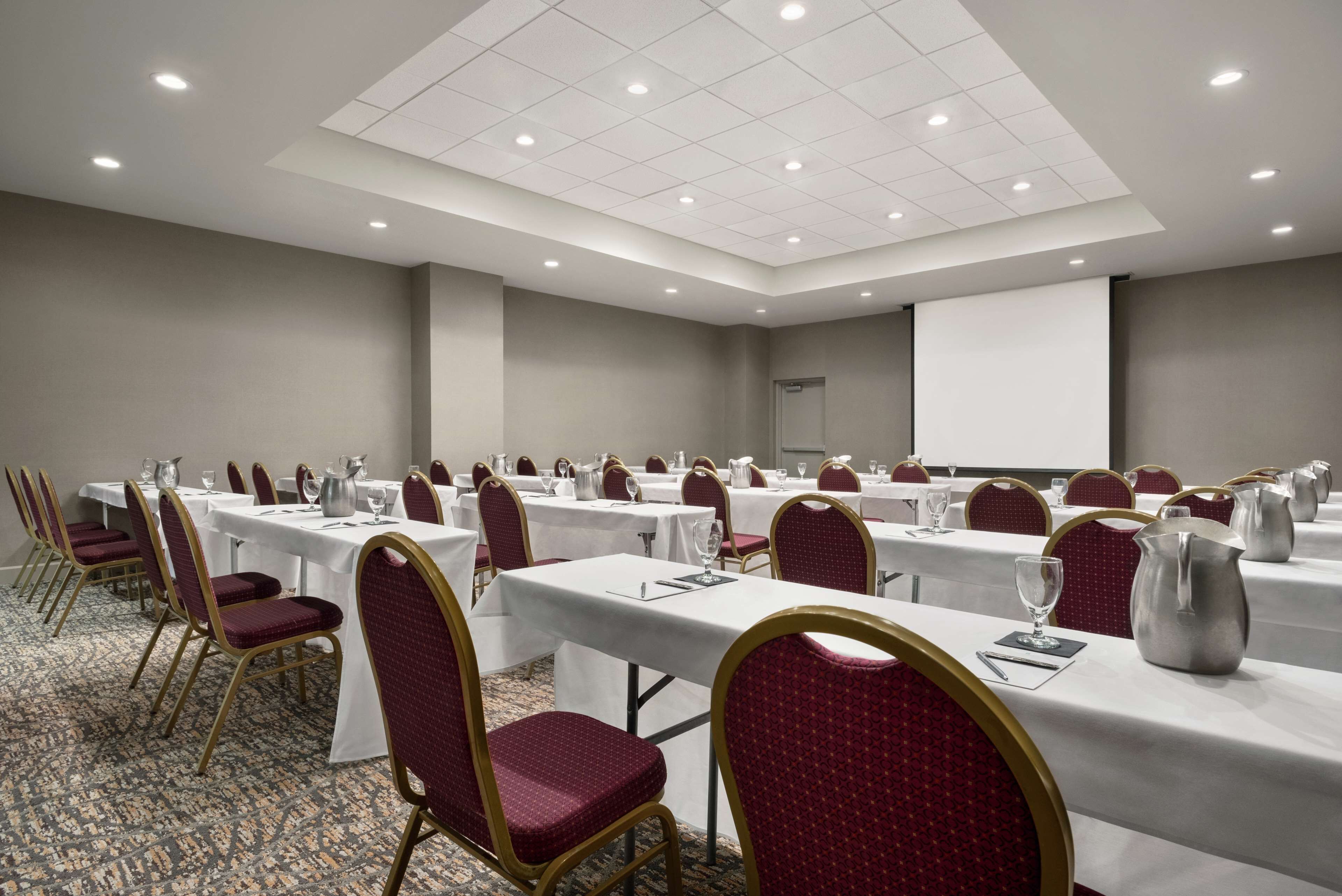 Un salón de conferencias con filas de mesas y sillas, equipado con tarjetas de identificación y jarras de agua.