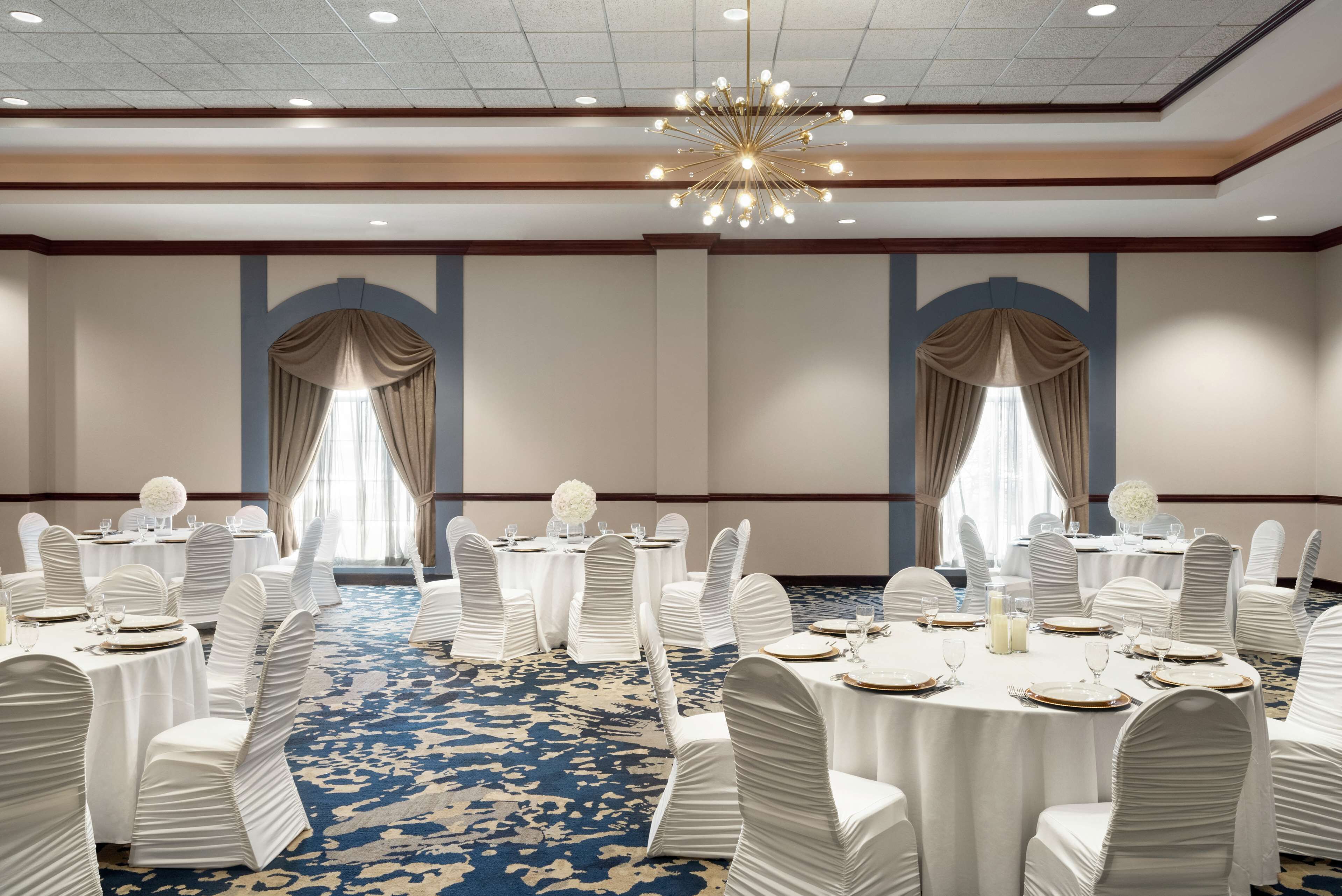 A banquet hall with round tables, white chairs, and chandeliers.
