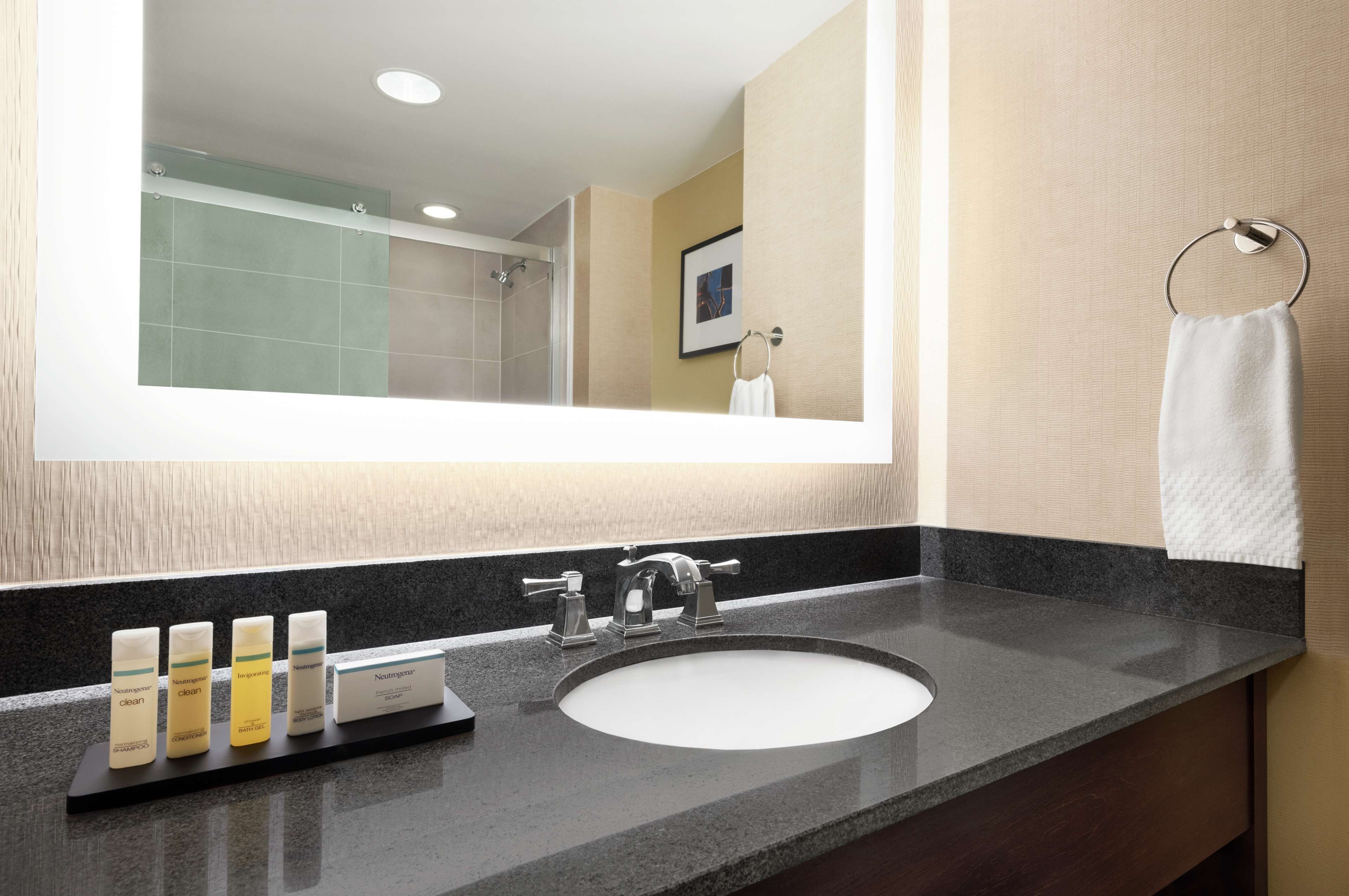 A bathroom with a large mirror, a sink, and a towel rack.