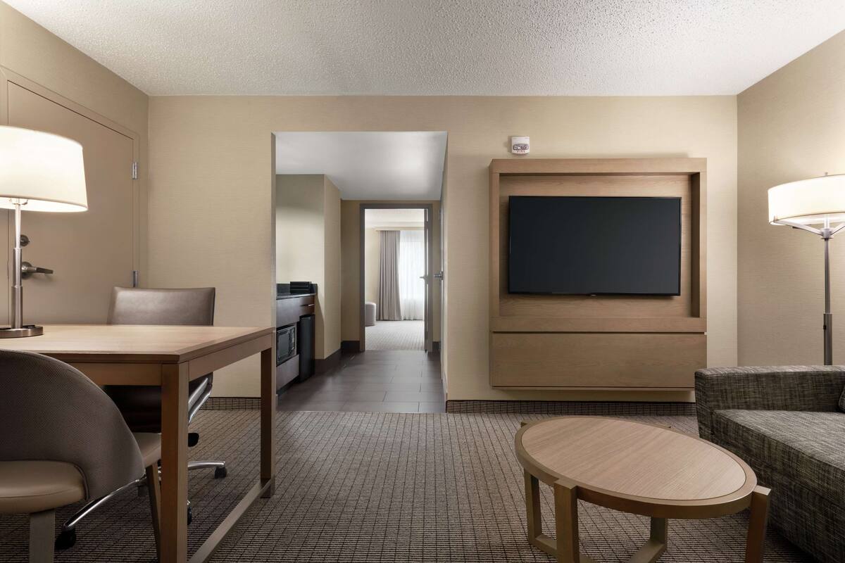 A hotel room with a bed, a desk with a chair, a television mounted on the wall, and a sofa.
