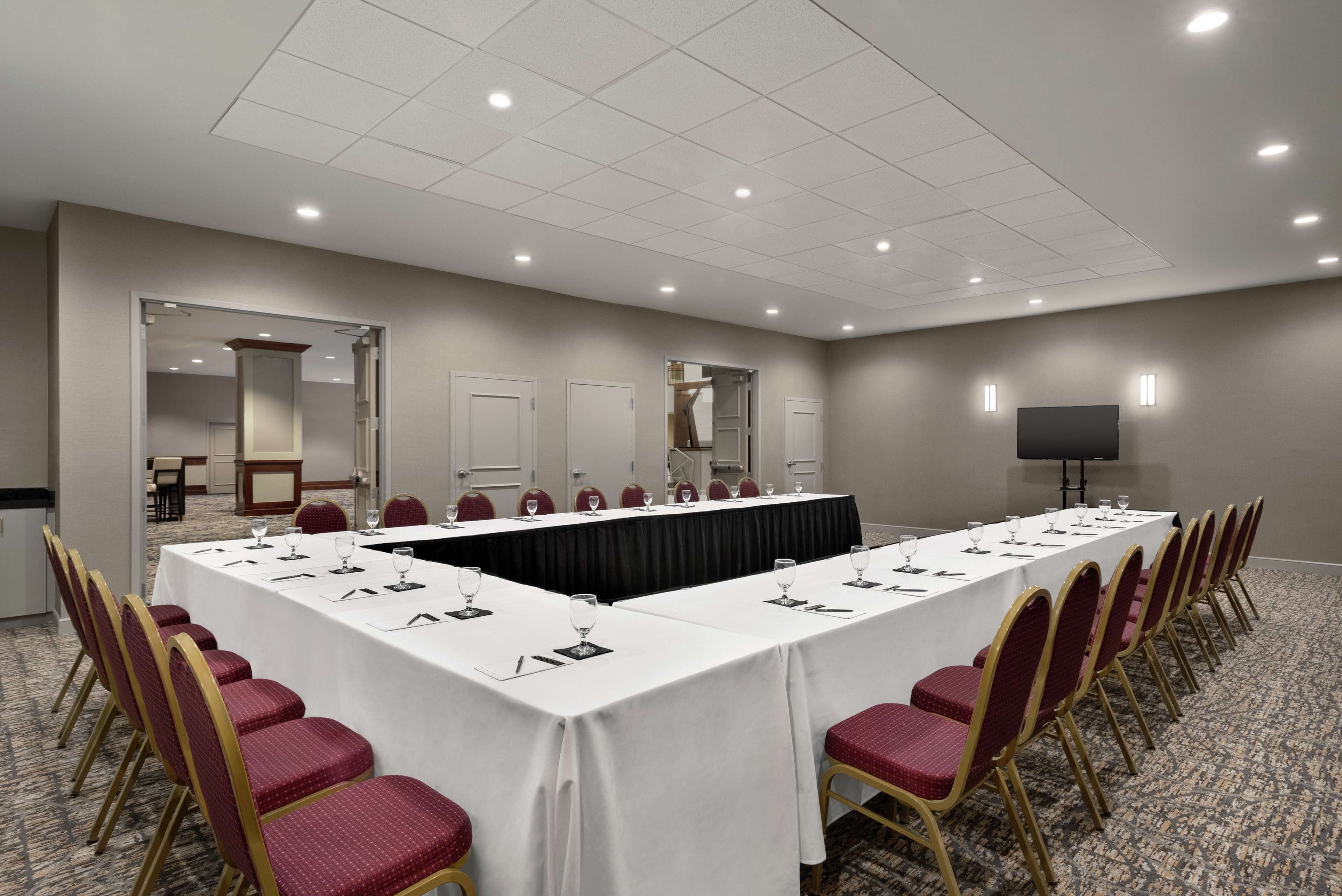 A conference room with a long table, red chairs, and a flat-screen TV.