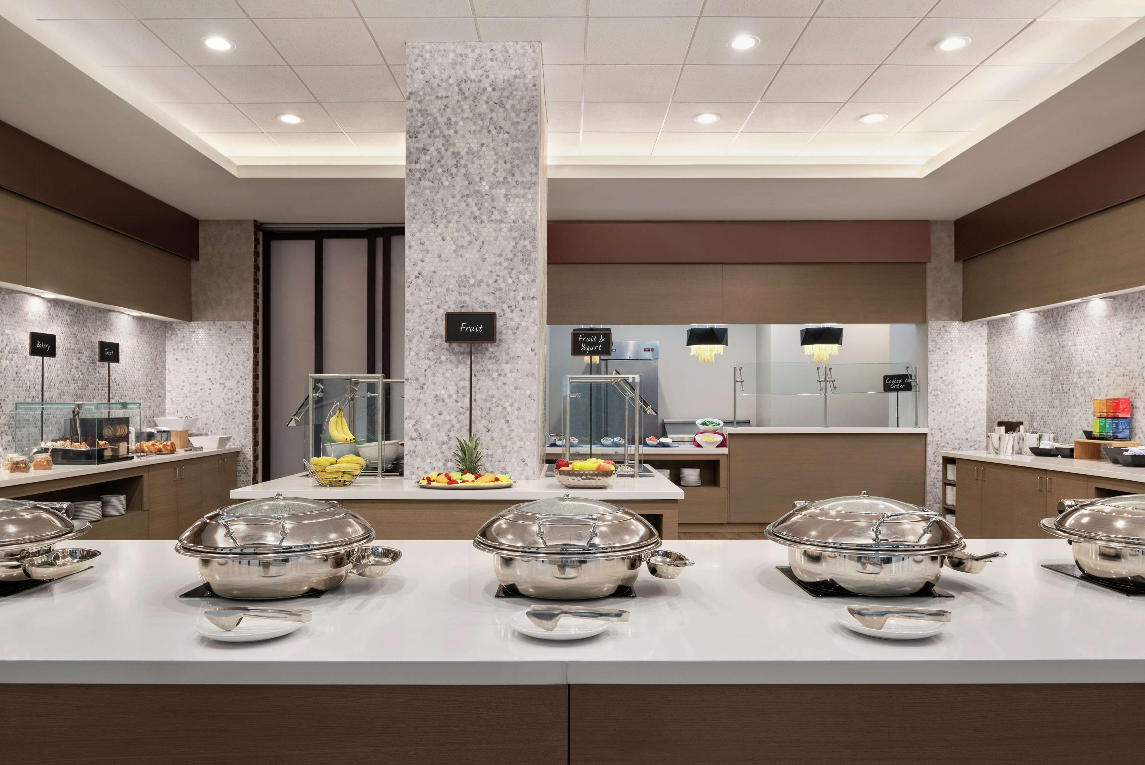 A modern hotel kitchen with buffet stations, a central pillar, and a clean, organized layout.