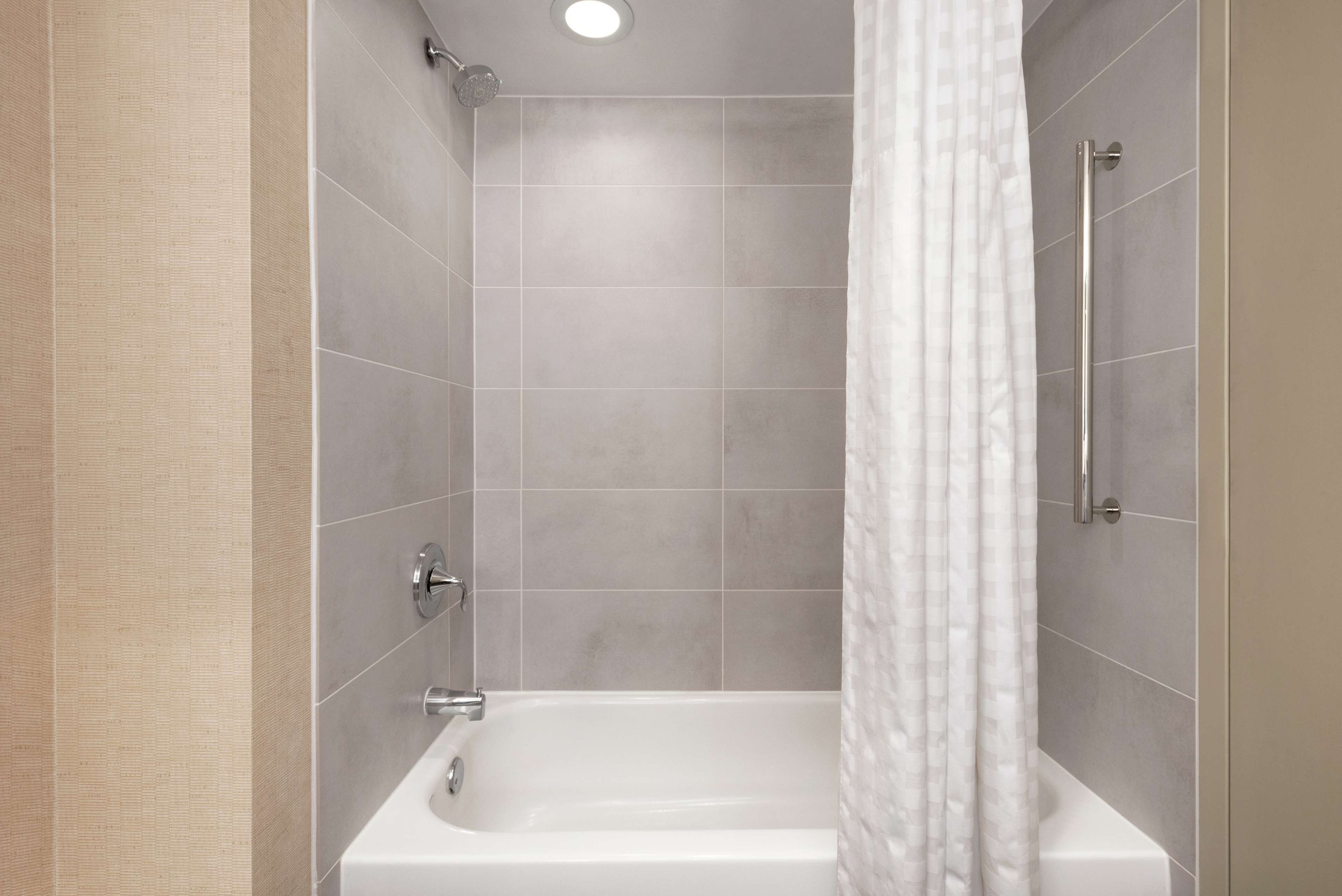 A modern bathroom with a bathtub, shower, and a handrail.
