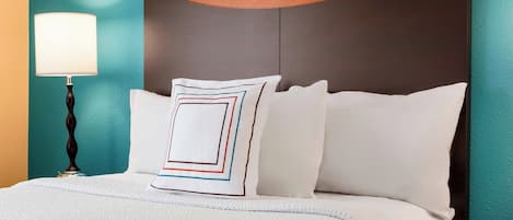 A neatly made bed with white bedding and a decorative pillow with geometric patterns, set against a teal wall with a wooden headboard.
