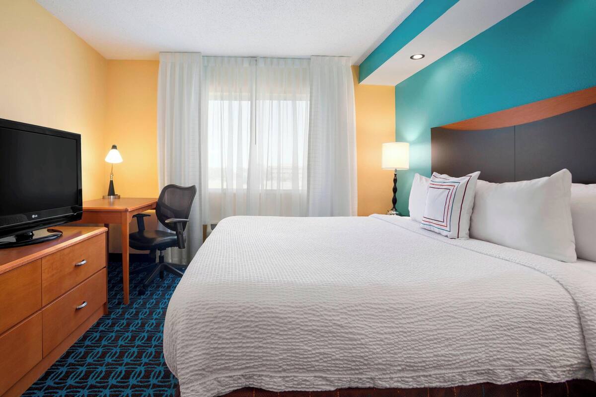 Una habitación de hotel con una cama grande, un escritorio con televisión, una silla y una lámpara.
