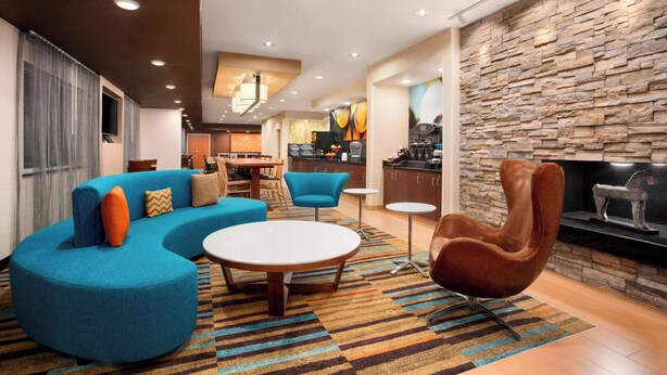 Una sala moderna con un sofá seccional azul, una mesa de centro redonda y un sillón marrón. Se observa un área de cocina al fondo con un salpicadero de pared de piedra.