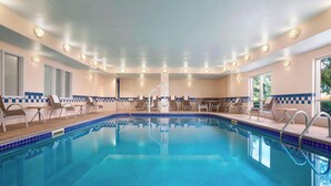 Una piscina con sillas de descanso y zona de sol, rodeada de ventanas y un suelo de baldosas.