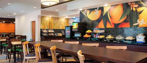 Un comedor de hotel con mesas y sillas de madera, una barra de buffet con diversos alimentos y un mural grande en la pared.