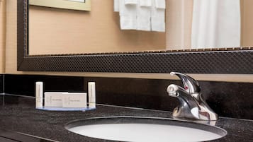 Un baño con encimera negra, un lavabo redondo y un espejo grande. Hay tres artículos de aseo sobre la encimera.