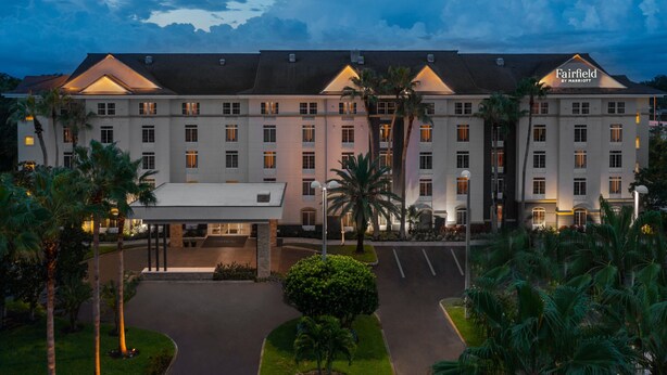 Un hotel de varios pisos con entrada central, palmeras y fachada bien iluminada.