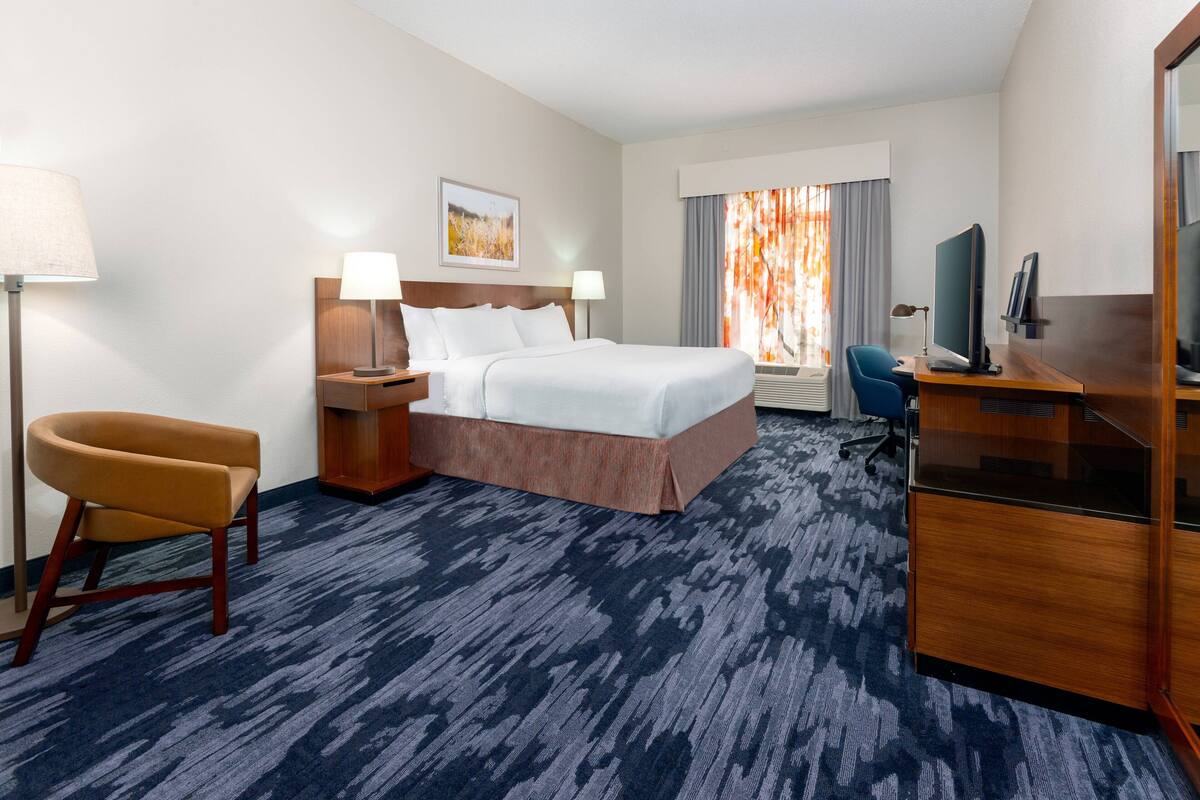 A hotel room with a large bed, a desk, a chair, and a television.