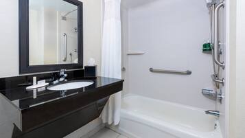 Un baño moderno con lavamanos de encimera negro, un espejo grande y una bañera blanca.
