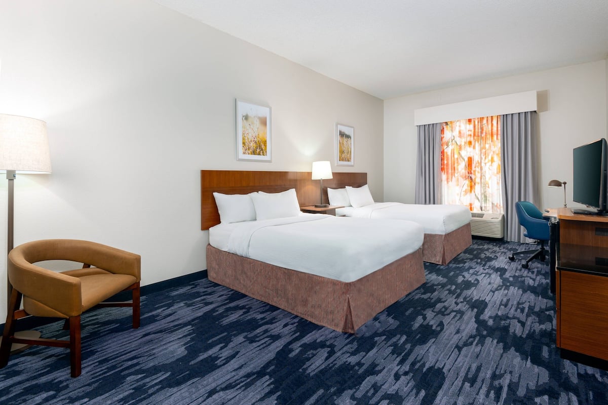 A hotel room with two beds, a desk, a chair, and a TV.