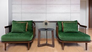 Dos sillones verdes tapizados, con estructura de madera y detalles en marrón, sobre un piso de baldosas, con una mesita redonda entre ellos.
