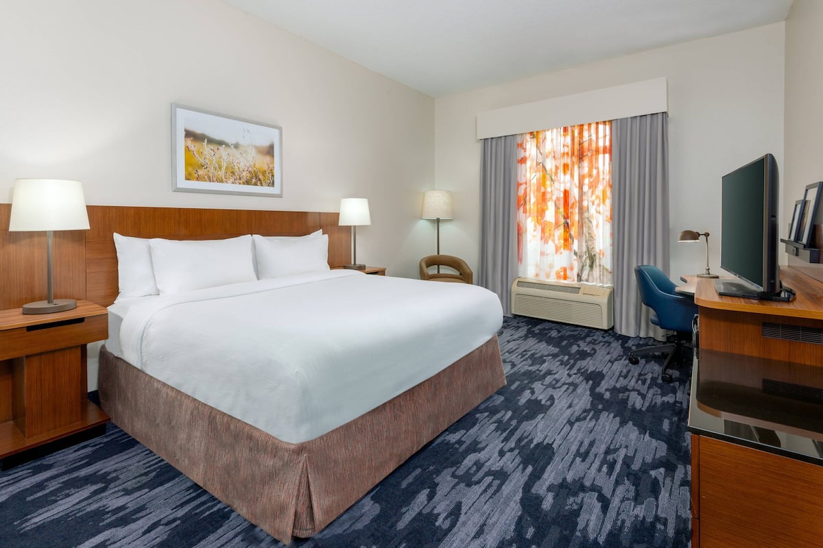A hotel room with a large bed, two bedside lamps, a desk with a computer, a chair, and a window with curtains.