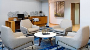 Un vestíbulo moderno con un mostrador de recepción, dos sillones, una mesita de café y un cuadro en la pared.