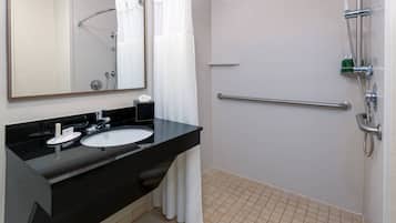 Un baño con un lavamanos negro, un espejo, ducha con pasamanos y suelo de baldosas blancas.