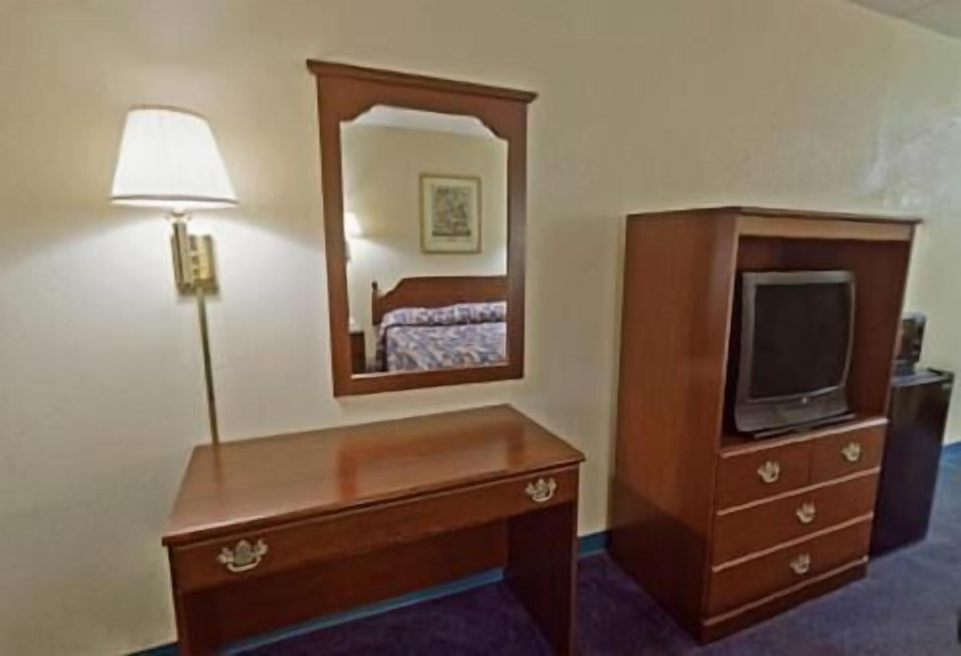 A wooden desk with drawers, a mirror, and a television on a stand.
