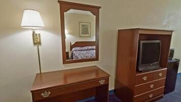 A wooden desk with drawers, a mirror, and a television on a stand.