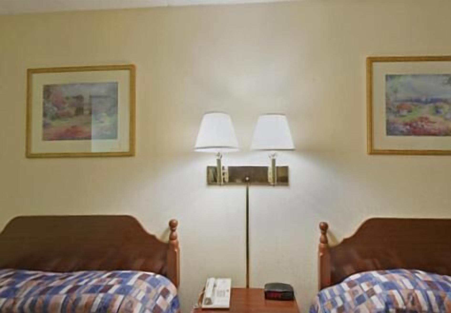 A hotel room with two beds, a nightstand, a lamp, and two framed pictures on the wall.