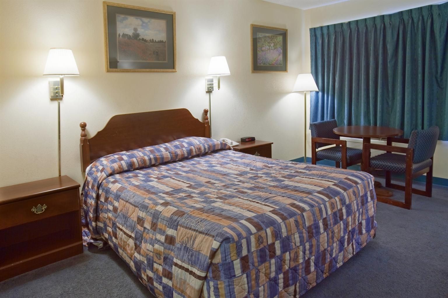 Una habitación de hotel con una cama grande, dos mesitas de noche, un escritorio con una silla y dos lámparas de pared.