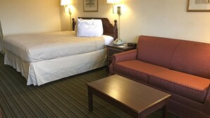 Une chambre d’hôtel avec un lit double, un canapé rouge, une petite table en bois et deux lampes de chevet.