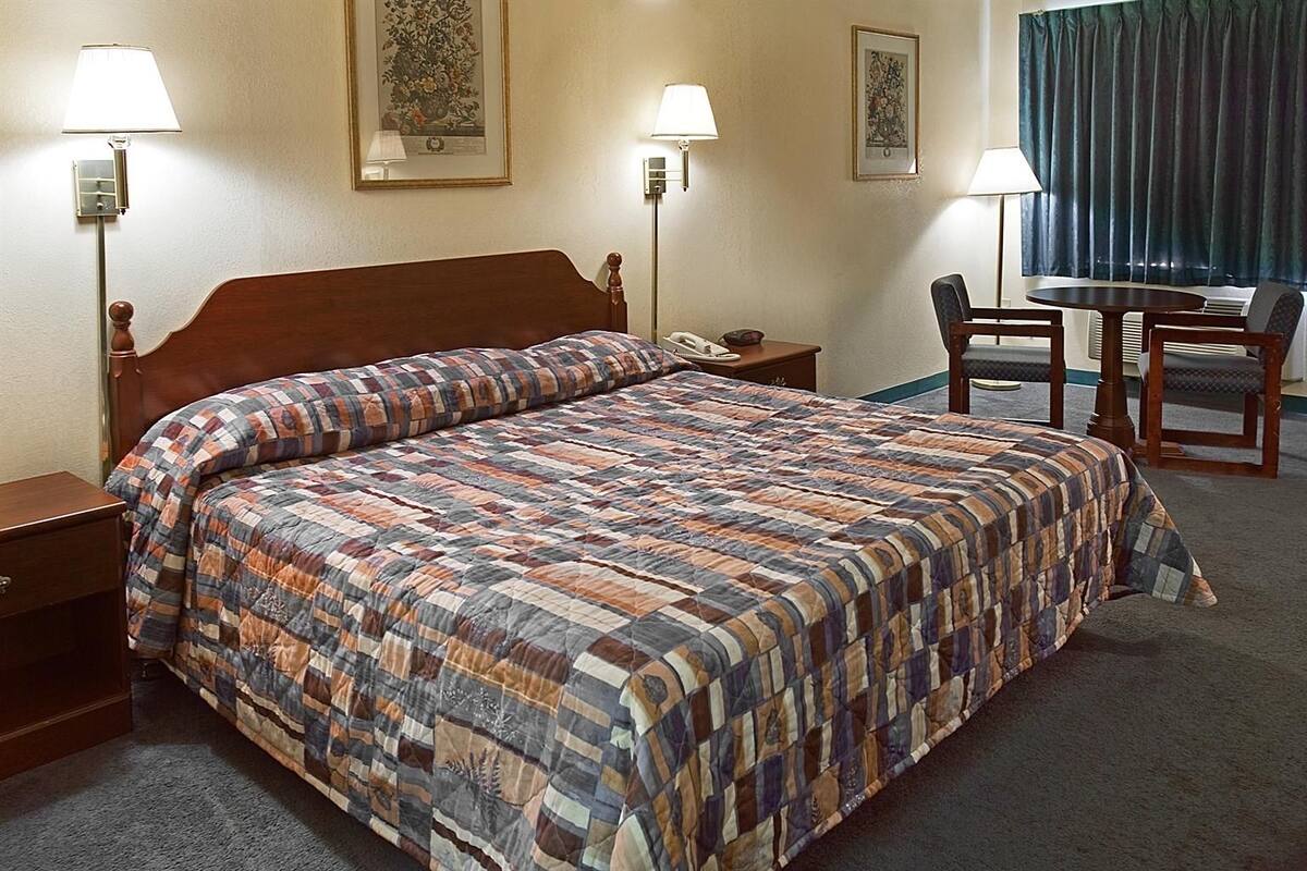 A hotel room with a large bed, two bedside lamps, a desk with a chair, and two framed floral artworks on the wall.