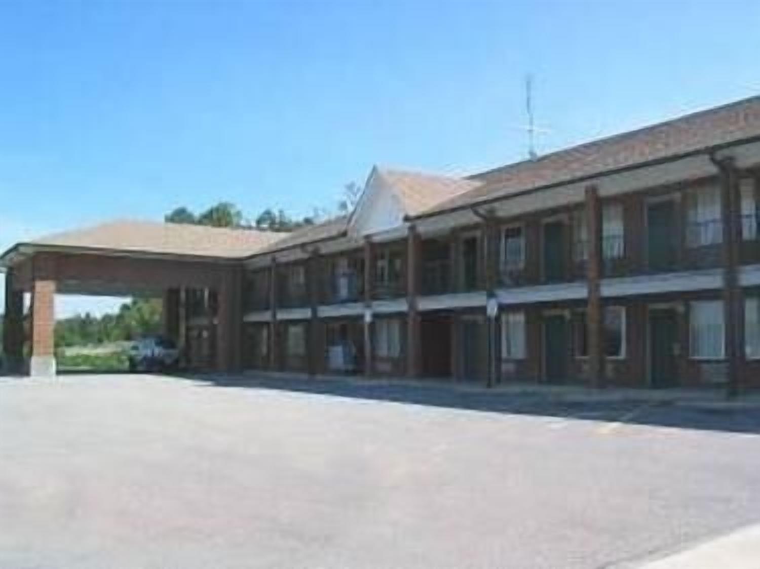 Un motel de dos pisos con zona de estacionamiento techada y un anexo de un piso.