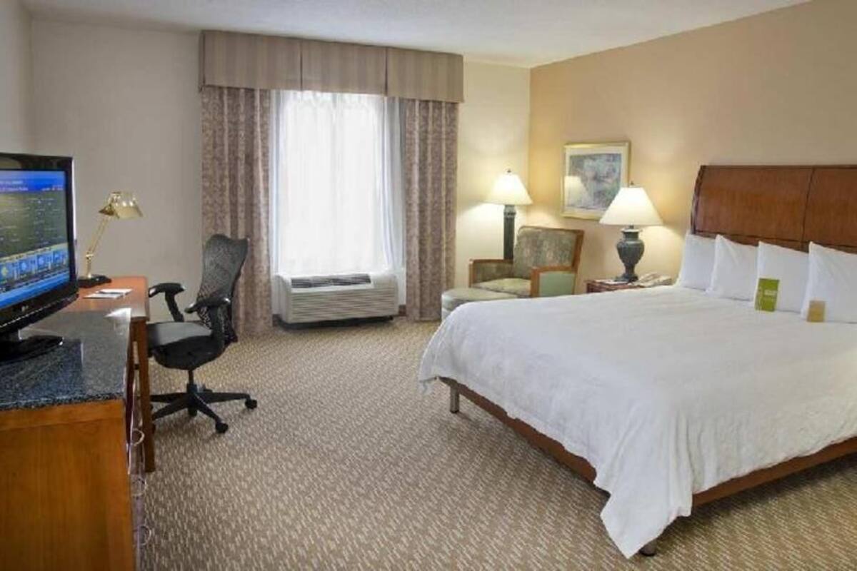 A hotel room with a bed, desk, computer, and two chairs.