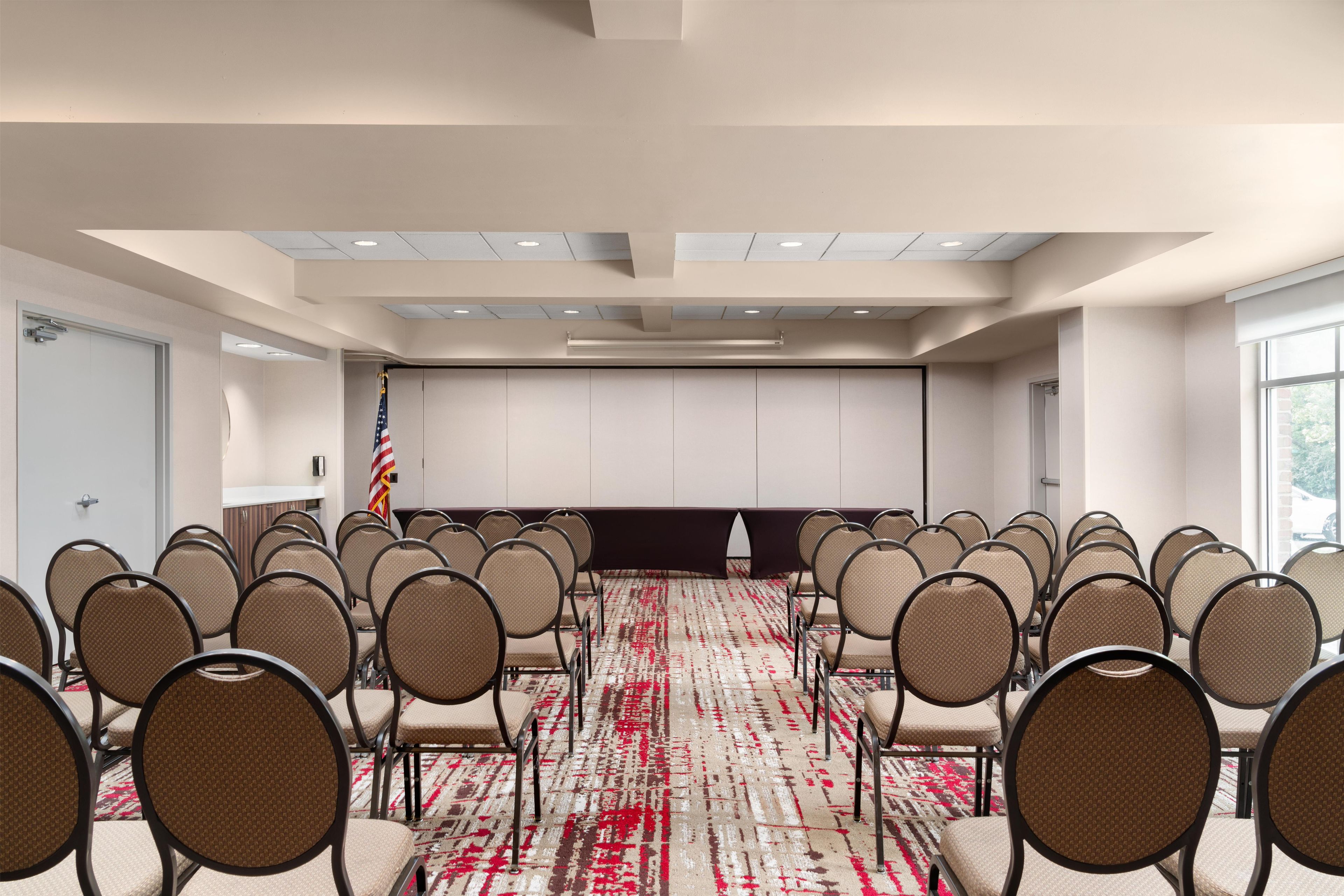 Een vergaderzaal met rijen stoelen, een projectiescherm en een Amerikaanse vlag.
