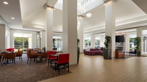 A spacious lobby with high ceilings, large windows, and a mix of seating areas including tables and sofas.