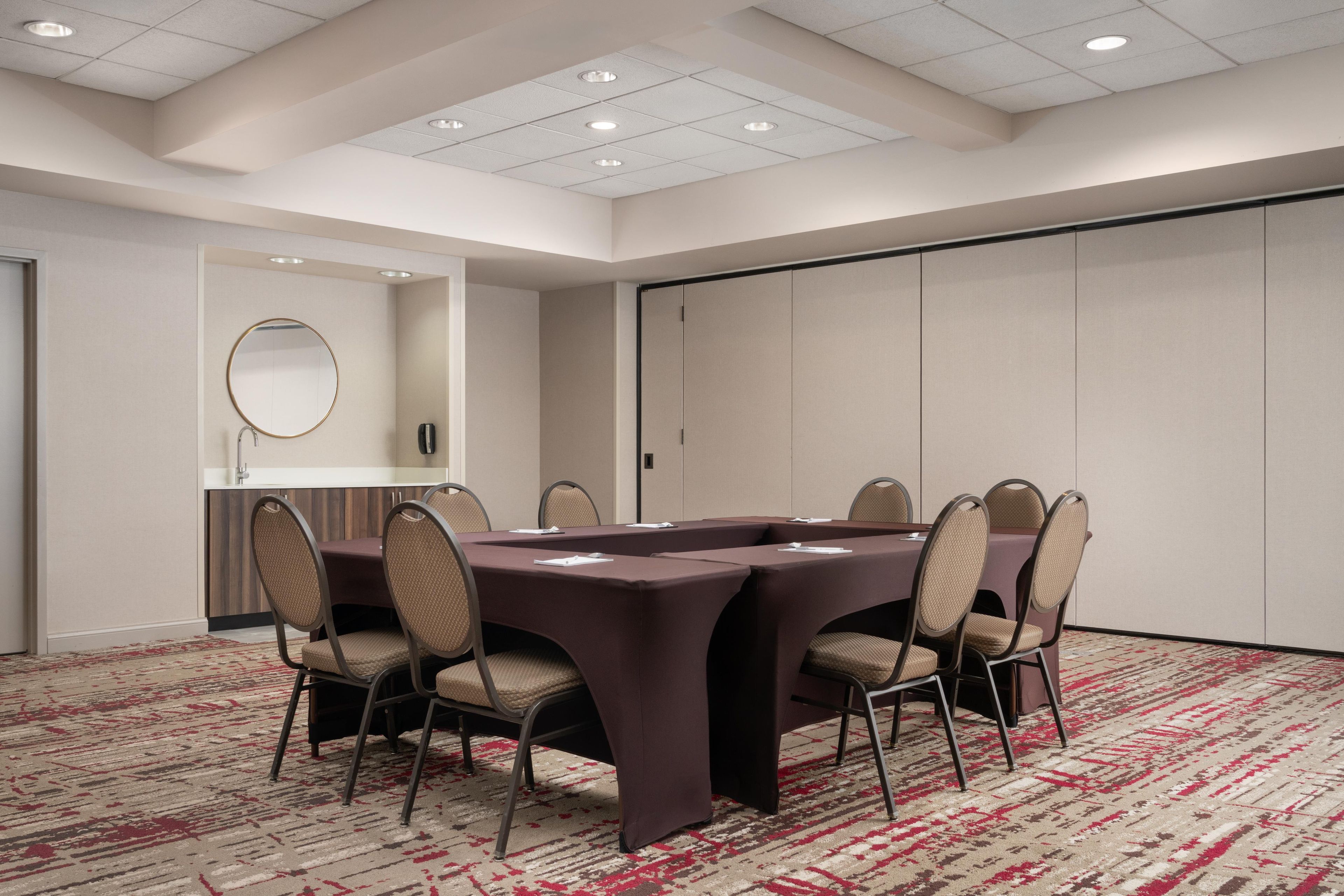 A conference room with a long table, chairs, a mirror, and a carpeted floor.