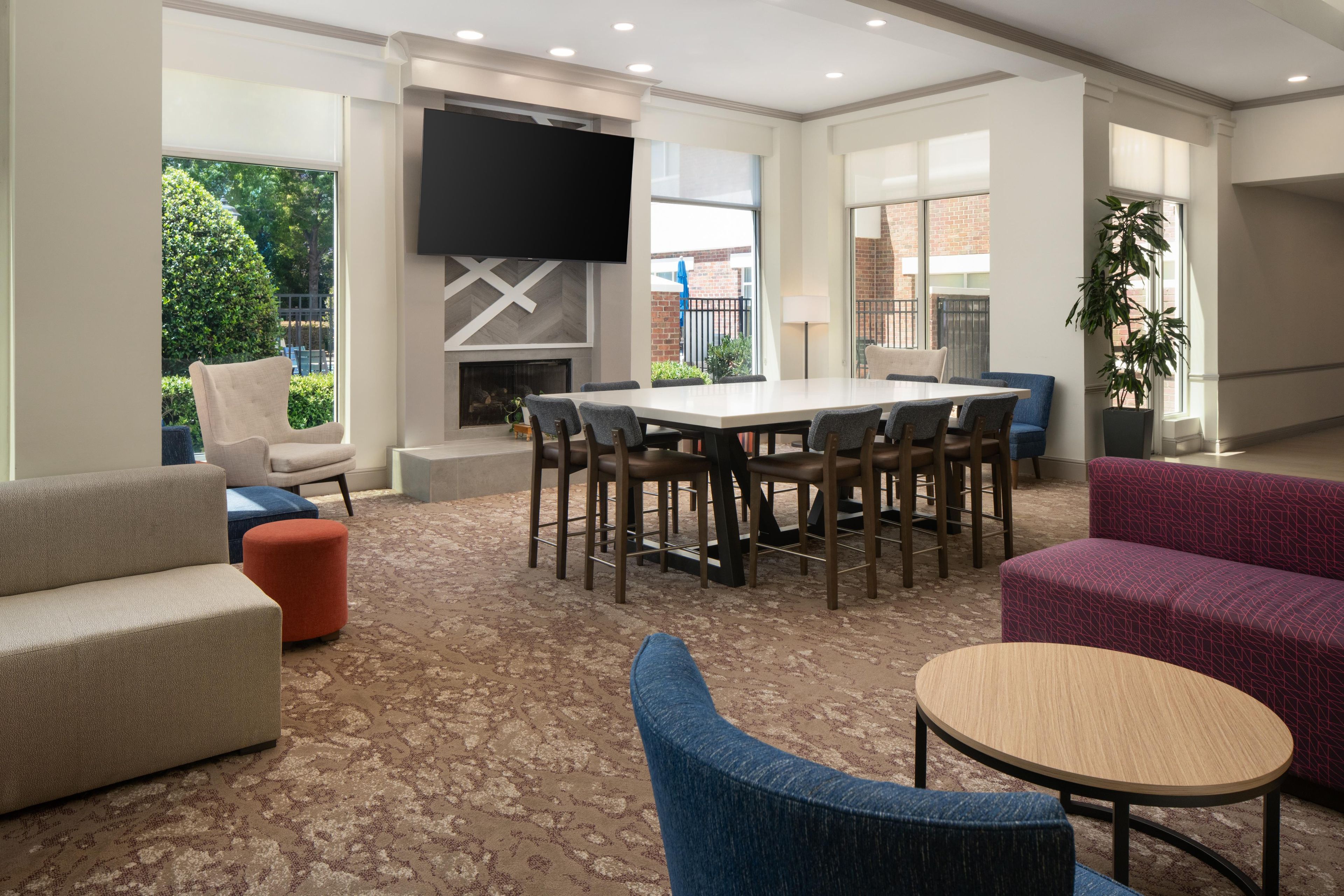 A modern meeting room with a large table, comfortable seating, a flat-screen TV, and a fireplace.