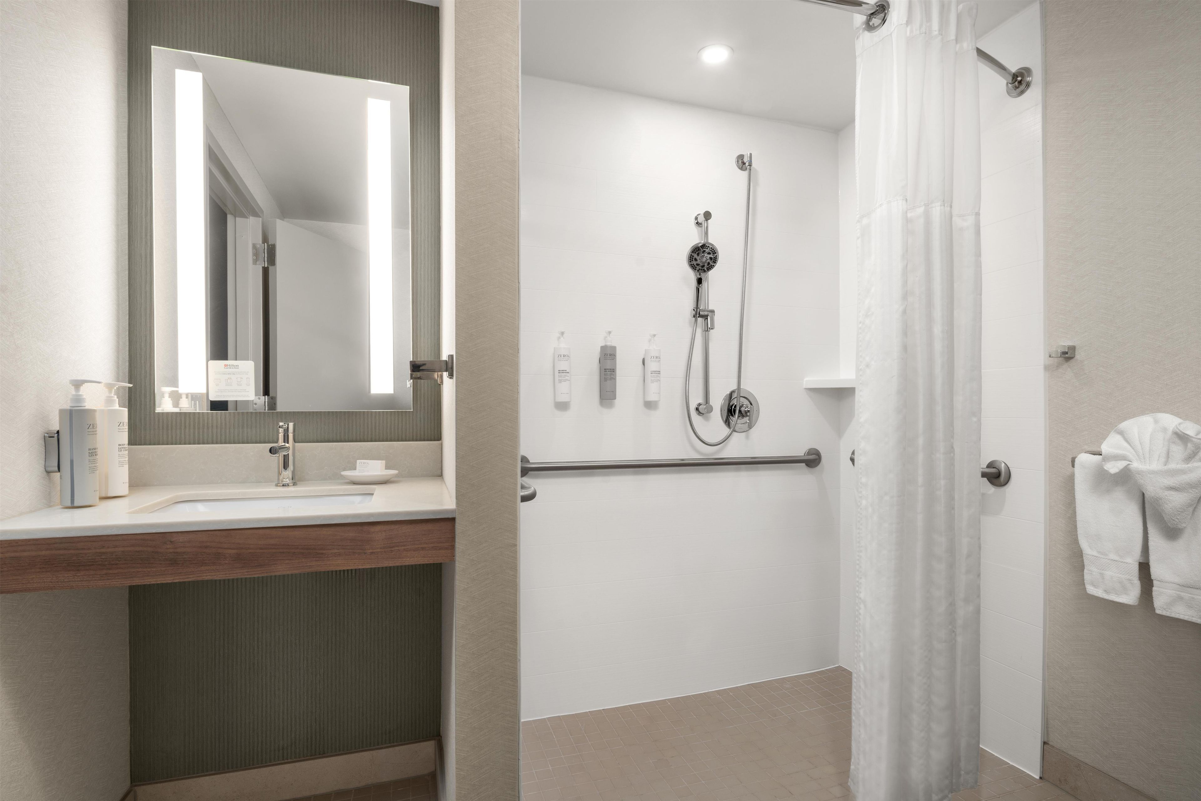 Un baño de hotel con ducha, lavamanos y espejo.
