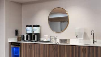 Casa de banho moderna com lavatório branco, espelho redondo e dois dispensadores de café identificados como 'Regular' e 'Descafeinado'.