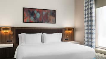 Quarto de hotel com uma cama grande, duas mesas de cabeceira, um quadro abstrato na parede e uma janela com cortinas.