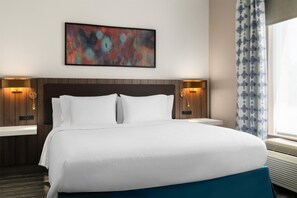 Habitación de hotel con una cama grande, dos mesitas de noche, un cuadro abstracto colgado en la pared y una ventana con cortinas.