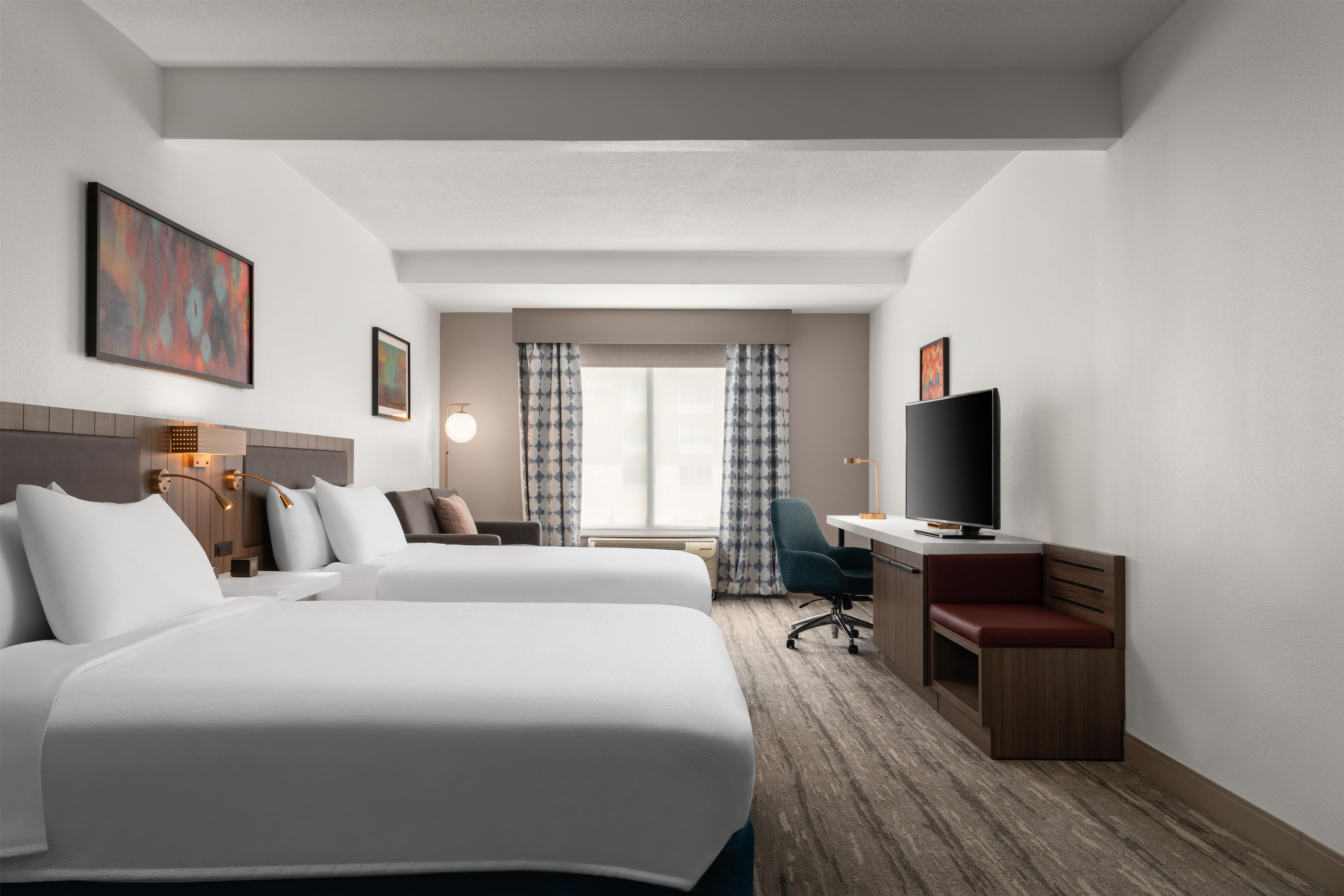 Ett hotellrum med två sängar, ett skrivbord, en tv och en stol.