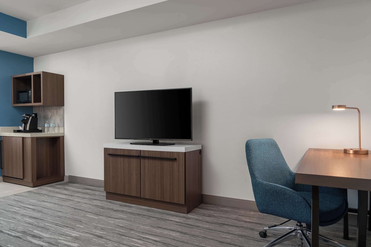 A modern room with a flat-screen TV on a wooden cabinet, a blue upholstered chair, and a desk with a lamp.