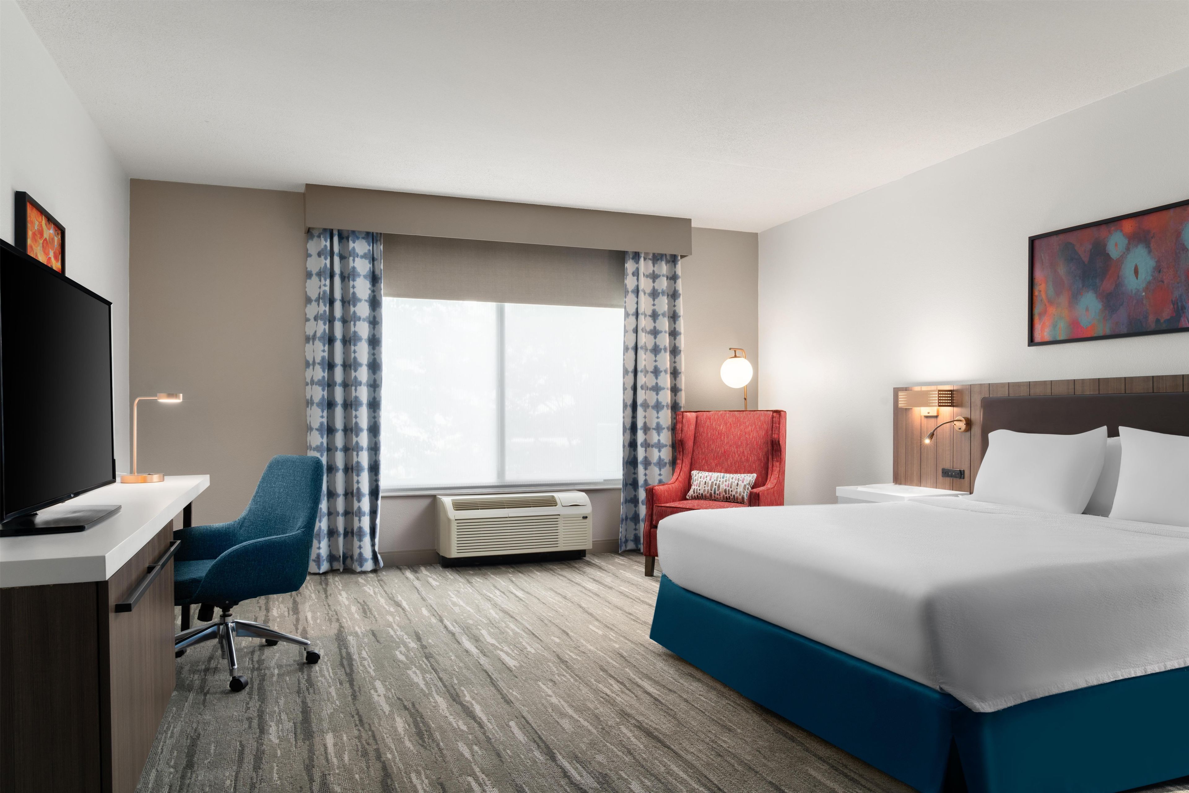 Ein Hotelzimmer mit Bett, Schreibtisch, Stuhl, Klimaanlage und Fernseher.